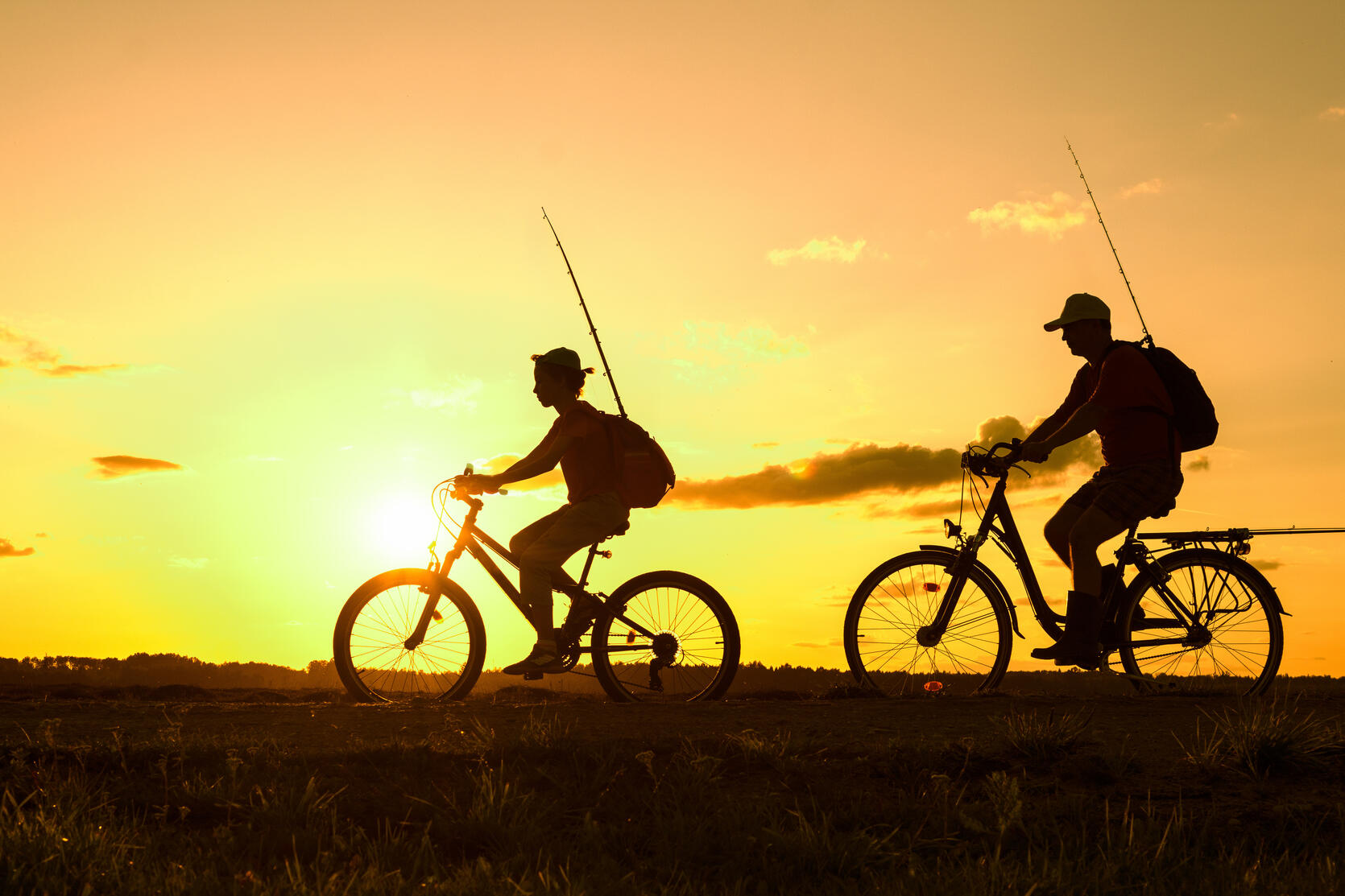 2 people on bikes with fishing rods at sunset