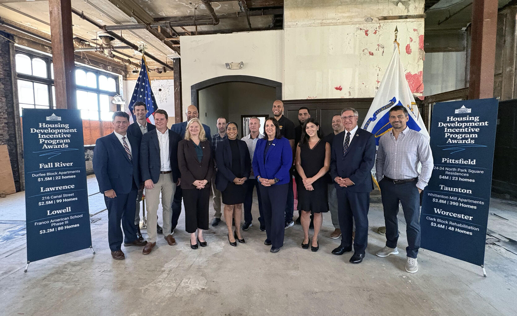 Healey-Driscoll Administration officials stand with representatives of communities receiving HDIP awards in an old mill building