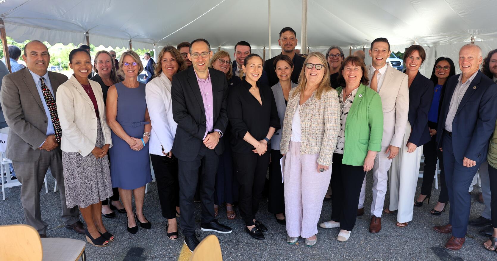 A group of state legislators, Healey-Driscoll Administration officials and grant recipients stand for a group photo under a large white tent.