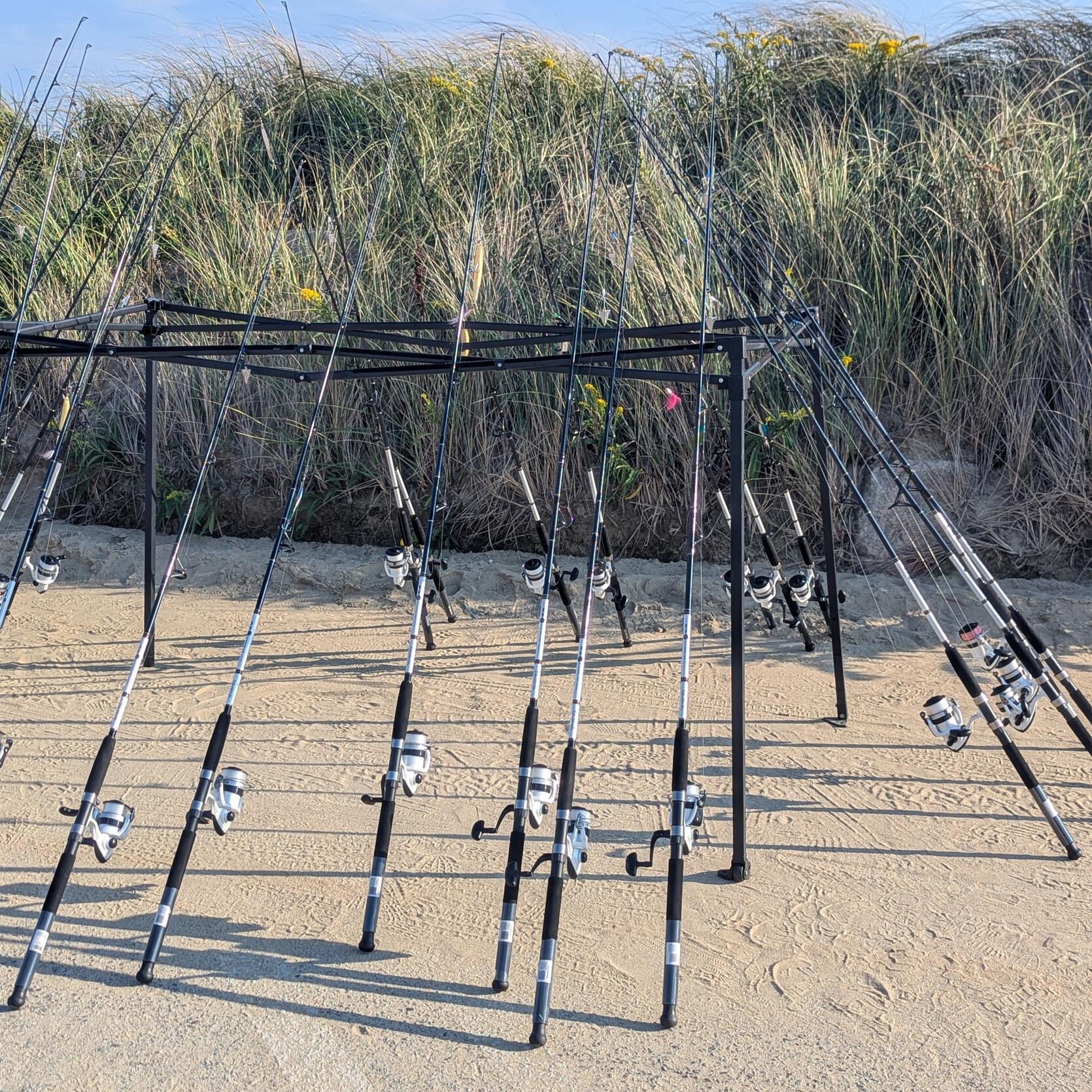 A collection of fishing rods and reels on a beach.
