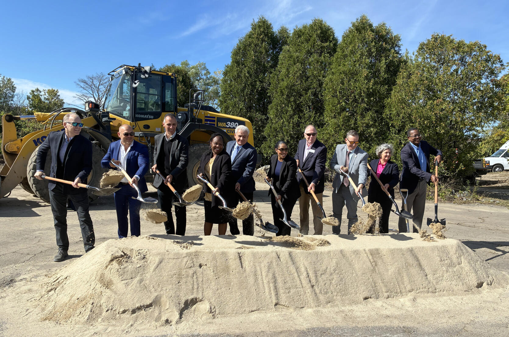 Officials in hard hats stand with shovels in hand behind a pile of dirt to mark the official groundbreaking for the development.