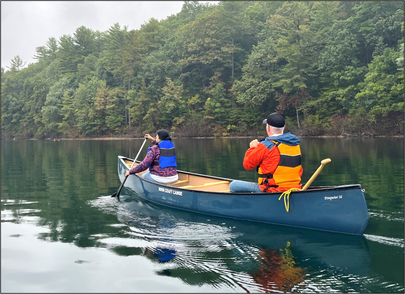 Two people are padding in a canoe on a lake in the woods. 