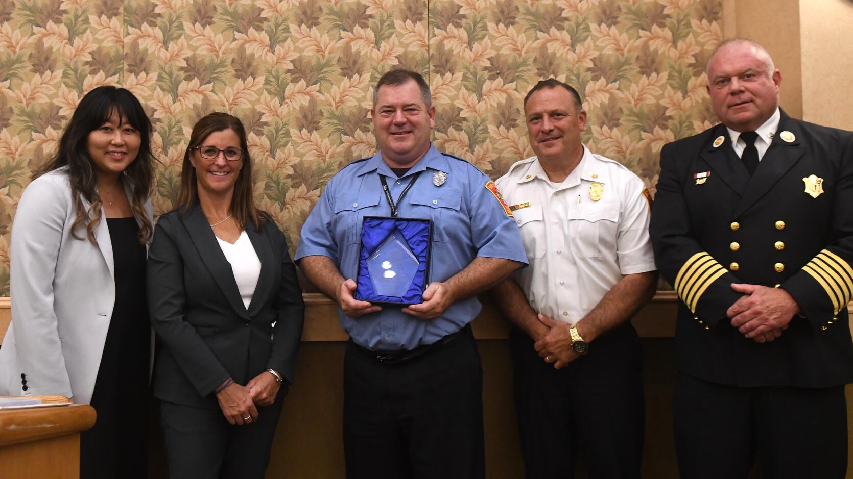Firefighter Peter Reardon holding the Educator of the Year Award with local and state officials
