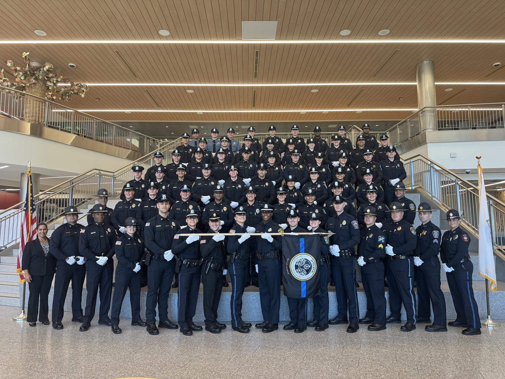 A large group of uniformed police officers stand on a staircase in a formal pose during a police academy graduation. 