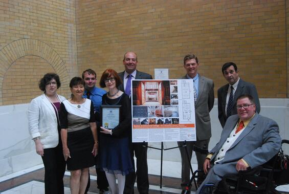 A group of people in business formal attire gathered around the display board for the project.