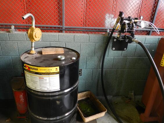 A black waste-collection barrel against a wall.