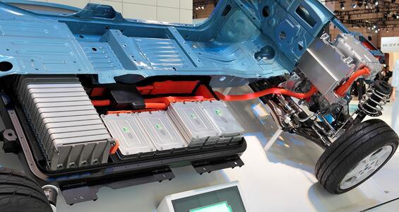 The underbody of an electric vehicle, with gray lithium ion batteries connected with orange indicator cables.