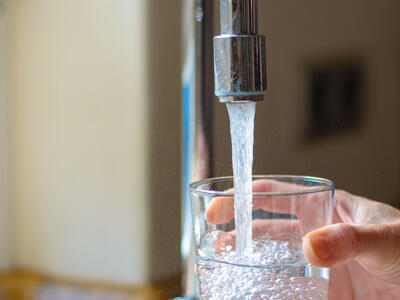 A woman's hand filling a glass of water at a faucet
