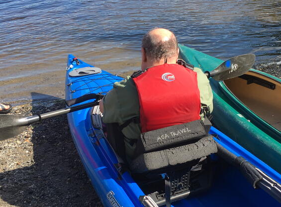 A paddler sits in a kayak holding a paddle. The paddler has two foam wedges between their back and the kayak seat back.