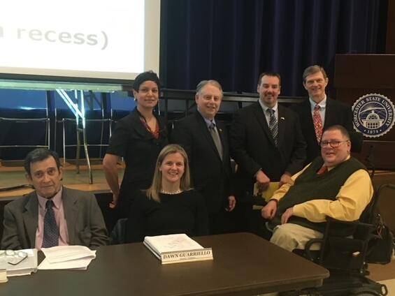 Tom poses with colleagues in front of a podium with the Worcester State University logo on it