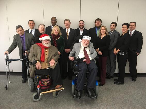 Tom poses with colleagues. He is wearing a Santa hat and red scarf.