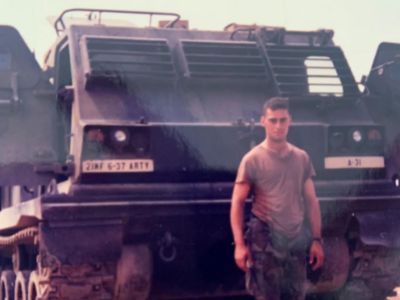 Richard Patchin stands in front of a military vehicle