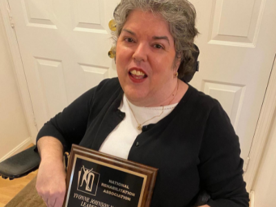 A woman poses in a chair as she holds an award