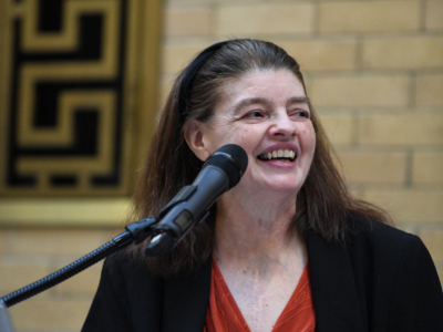 A woman with brown hair smiles as she speaks into a microphone
