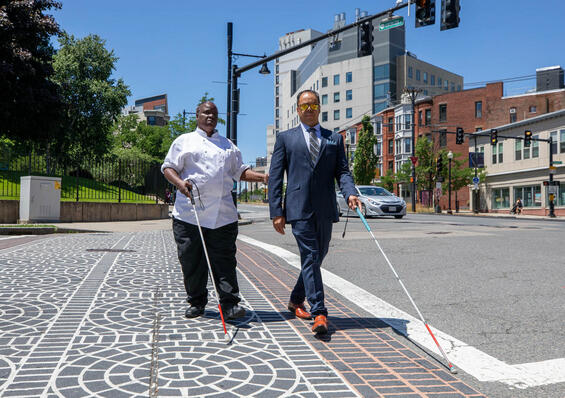 Two people walking in a crosswalk while using their white canes