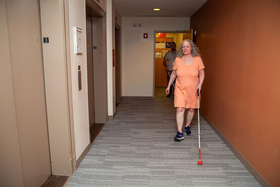 Woman walking with her white cane in the carpeted hallway of an office