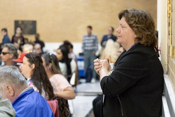 The sideview of a woman clasping her hands while watching the ceremony from the back of the Great Hall.