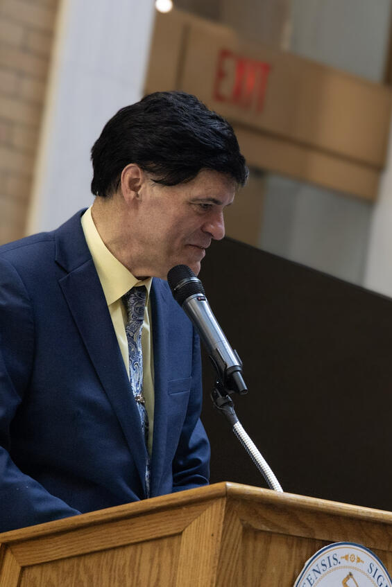 A man in a suit standing behind the podium and reading braille.