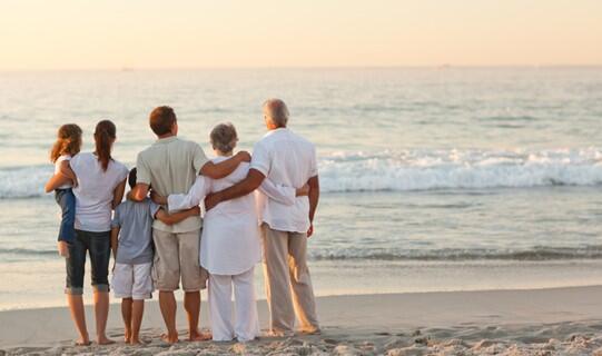 Family of six on the beach looking at the waves with their arms around each other
