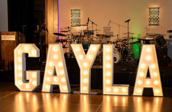 Large illuminated “GAYLA" letters in front of a stage with musical instruments in a ballroom. 