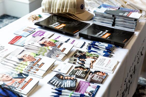 A stack of promotional materials such as pamphlets, flyers, pens, caps, magnets.