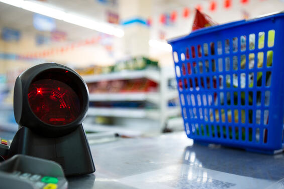 Grocery store check out counter with a round price scanner on the left, and a blue shopping basket on the right.