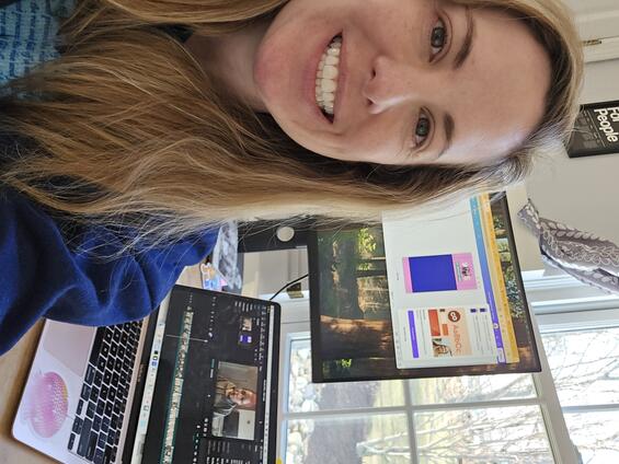 Kelsey Oates sitting in front of a laptop and computer monitor editing a video.