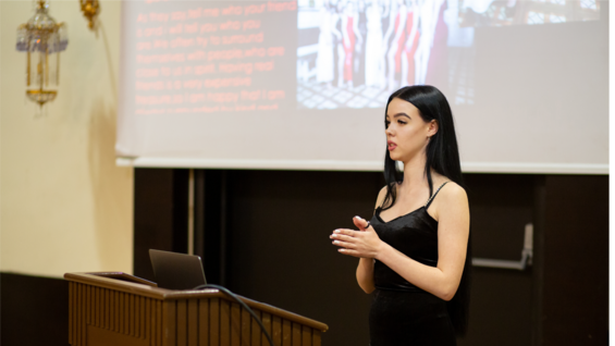 A woman presents at a podium with slides projected behind her