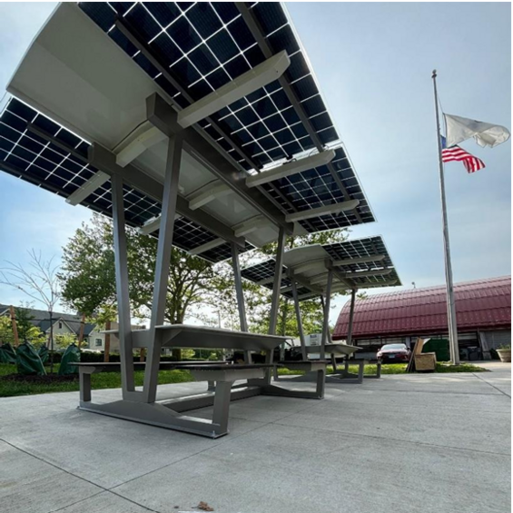 A photograph of benches beneath raised solar panels making up the solar shelter.