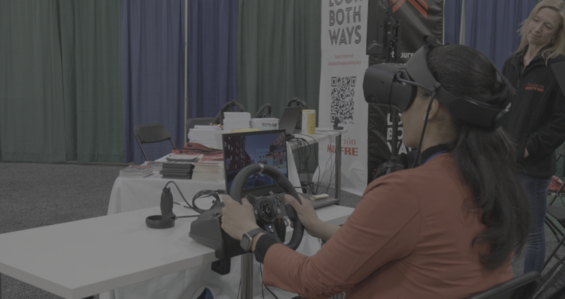 A person with a virtual reality headset and steering wheel. 