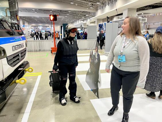 A woman in an age suit walks with a piece of luggage.