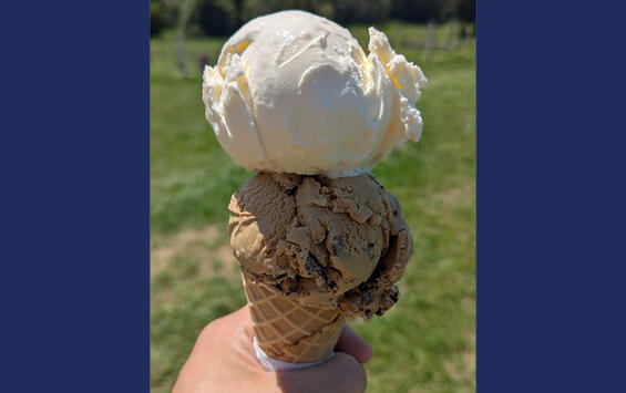 A person's hand holding a sugar cone with two scoops of ice cream.