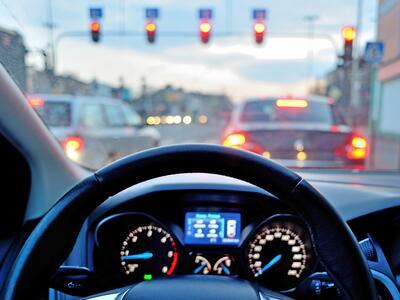 The dashboard of a car, showing the steering wheel and traffic lights ahead.