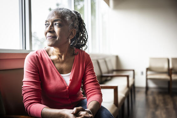 Woman of color sitting in a chair, looking out a window.