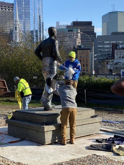 Workers unwrap the JFK statue in its new location