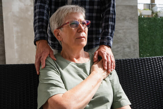 Woman sitting with someone's hands on her shoulders providing comfort