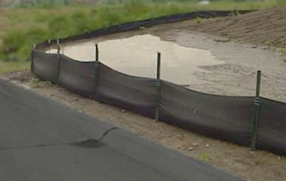 Muddy water being held back by a silt fence held in place by stakes.