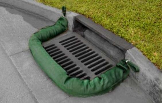 A green compost filter sock surrounds a storm drain along side a curbed street.