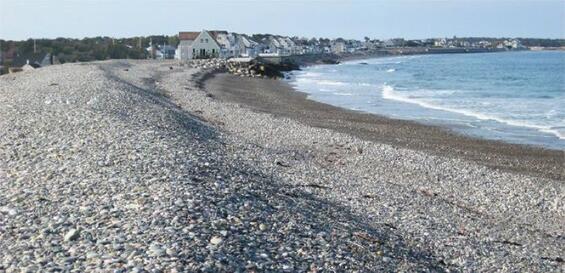 A large and well-formed cobble dune in the foreground with cottages and the ocean in the back