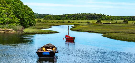 A tidal river with salt marsh and two boats moored in the foreground.