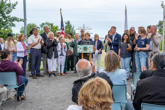 Governor Healey standing outside at a podium surrounded by happy people.