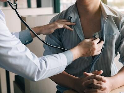 A person at a doctor's office having their heart checked by a doctor with a stethoscope. 