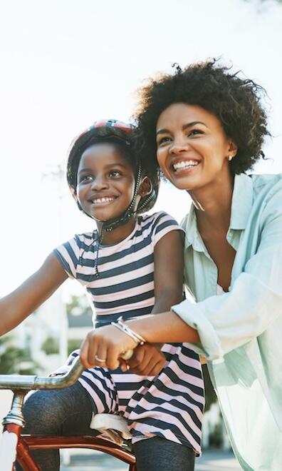 A child riding a bike outside with support from a parent.