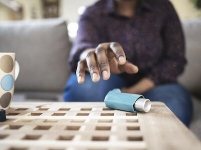 An adult sitting on a couch reaching for their inhaler.