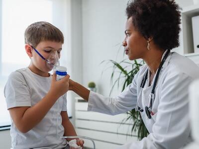A child in a doctor's office using an inhaler with help from a doctor.