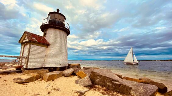 A sailboat sails by a lighthouse on Nantucket