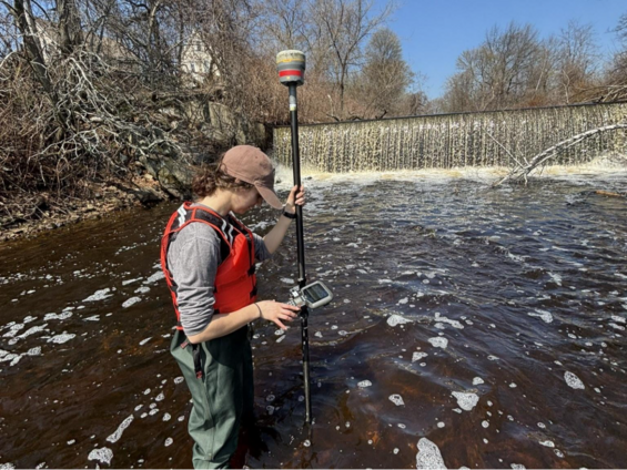 A person measures water quality downstream of a dam in a river.