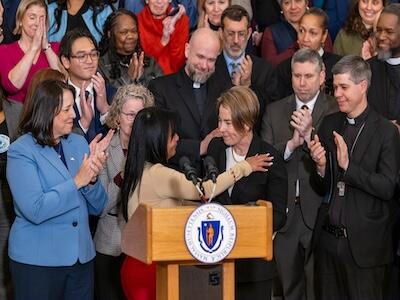 Governor Healey standing at a podium hugging a woman