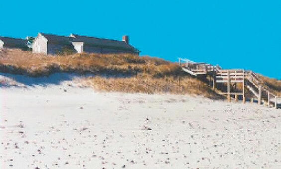A house and a wooden walkway over a dune. The dune has visible erosion and slumping. Sand has been added to the eroded area and planted with grass
