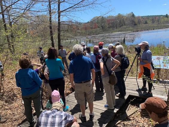 A group of hikers near a wetland listening to a conservation agent give a speech.